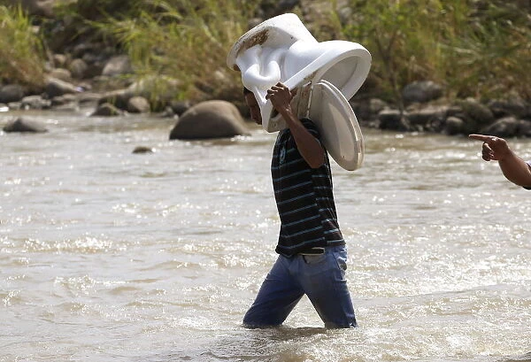 A man carries a toilet as he crosses the Tachira river border into Colombia