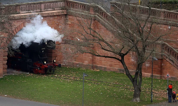 A man and his children look at a historic steam engine passing by on the museum rail