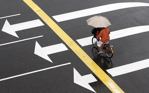 A man crosses an intersection on his bicycle while holding an umbrella as it rains