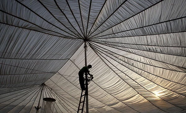 A man fixes lights on the pole of a tent set up for a wedding ceremony in Lahore