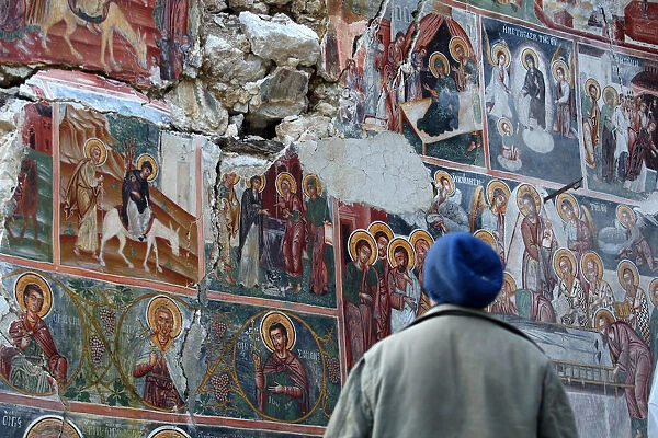 A man looks at a damaged fresco in The Orthodox Church of Saint Athanasios in Leshnica