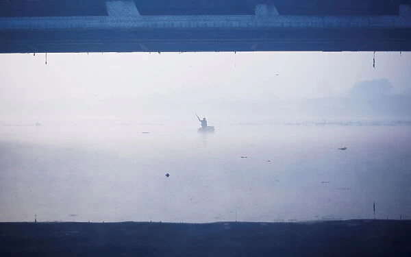 A man paddles a handmade boat across the Yamuna river on a foggy winter morning in