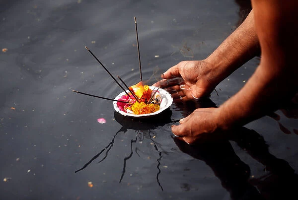 A man places an oil lamp in the polluted river Yamuna after offering prayers