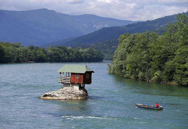 A man powers a boat near a house built on a rock on the river Drina near the western