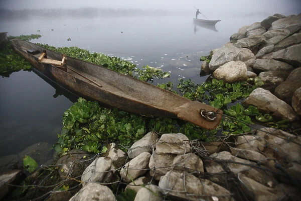 A man pushes his boat with the help of a bamboo stick to reach the bank of Rapti River at