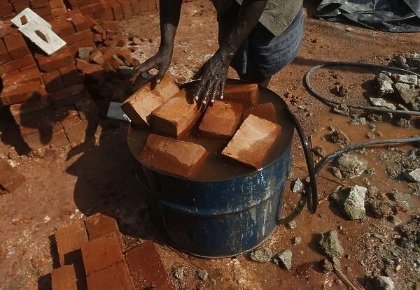 A man puts bricks into an oil barrel which filled with water at a construction site in