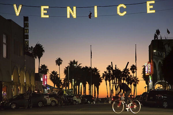 A man rides a bicycle under the Venice sign on Windward Avenue in Venice, California