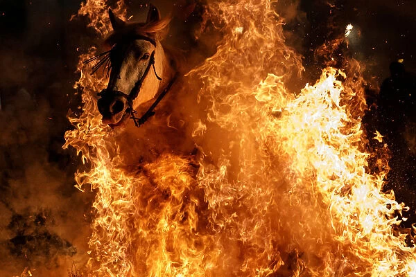 A man rides a horse through flames during the annual Luminarias celebration on the eve