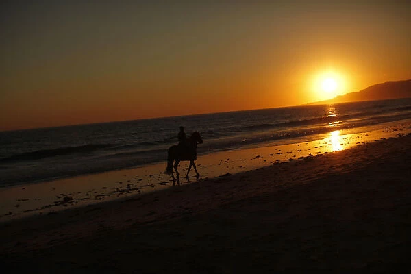 A man rides his horse along the shore on Los Lances beach during sunset in Tarifa