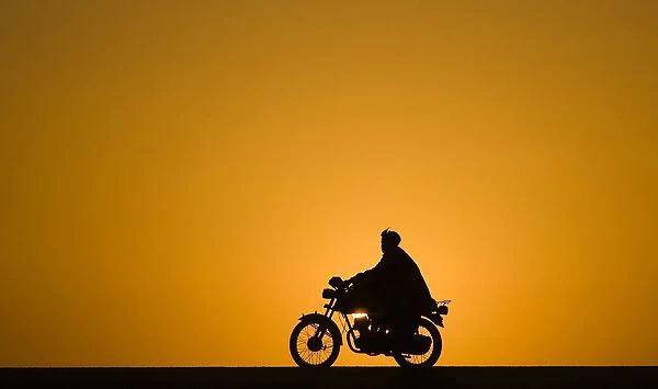 A man rides a motorcycle as the sun sets at Delaram district in Nimroz province