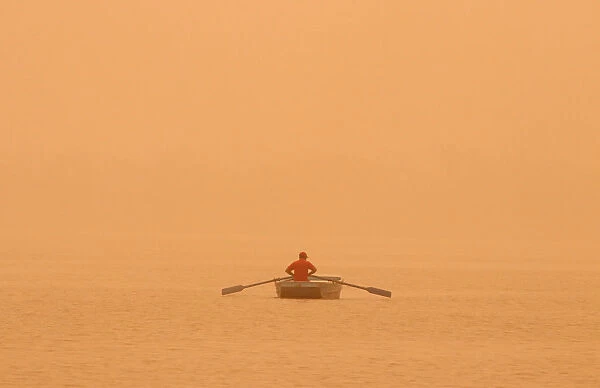 A man rows a boat amidst haze and dust in the waters of Sukhna lake in Chandigarh