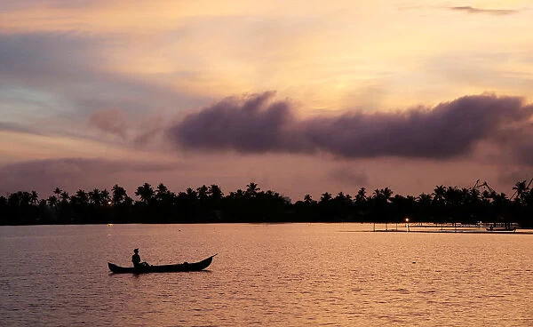A man rows his boat in the tributary waters of Vembanad Lake against the backdrop of