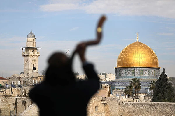 A man is silhouetted while he blows a Shofar, a ram horn, as the Dome of the Rock