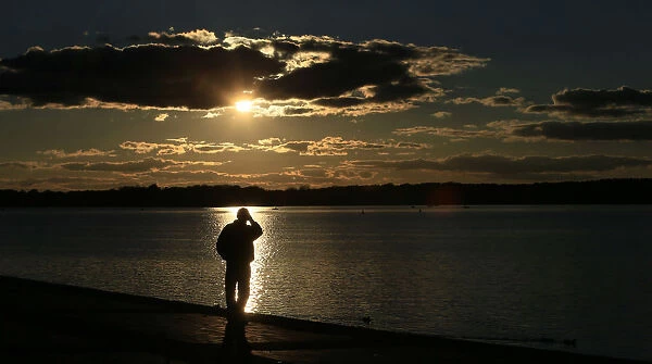 A man is silhouetted against the reflection of the sun in lake Tegel on a sunny autumn