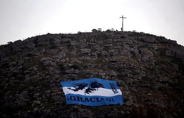 A man stands next to a cross as an Argentine national flag with an image of the Falkland