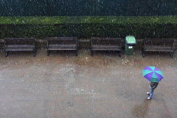 A man stands under an umbrella as rain stops play at the Wimbledon tennis championships