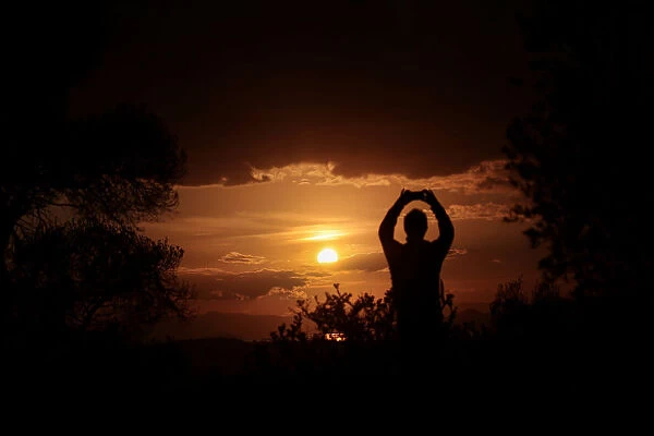 A man takes a picture of the sunset atop Filopappou hill in Athens