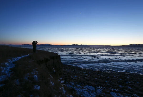 A man takes pictures from a bank of the frozen Yenisei River outside the village of