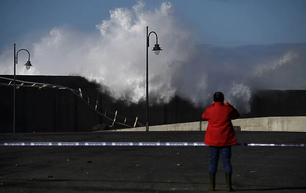 A man takes pictures of waves as they crash against a the port town of Puerto de Vega