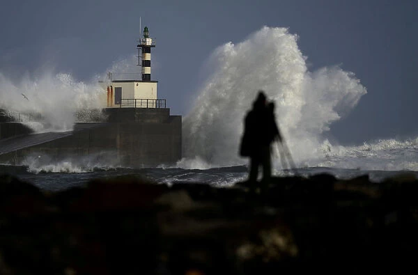 Man takes pictures of waves crashing at the San Esteban de Pravia seafront of the Spanish