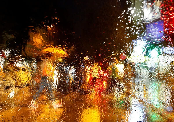 A man with an umbrella is seen through a car window covered with raindrops as he walks