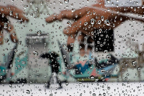 A man with an umbrella is seen through rain drops on a car window walking by a mural in