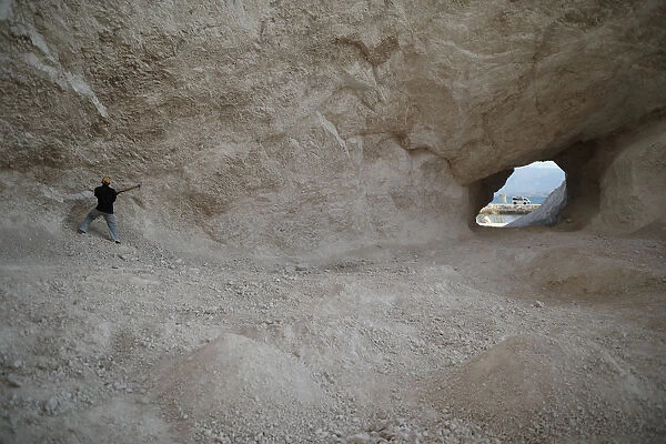 A man uses a pick to break rocks and get sand in a sand mine on the outskirts of Fond