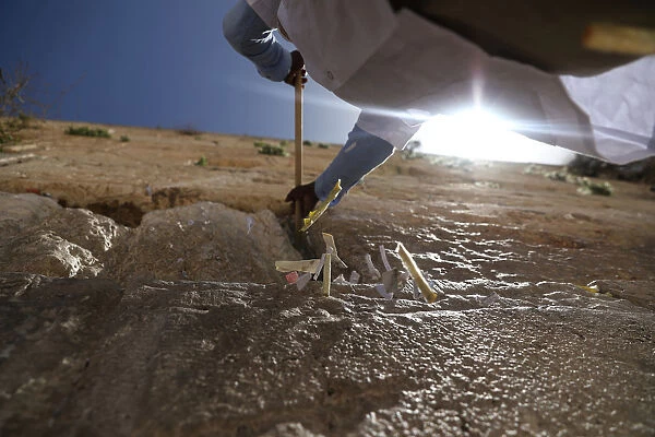 A man uses a stick to clear notes placed in the cracks of the Western Wall