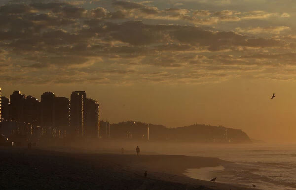 A man walks in Barra da Tijuca beach during the sunrise in Rio de Janeiro