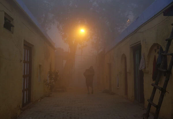 A man walks out of his house in an alley on a cold and foggy morning in New Delhi