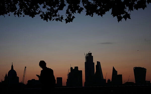 A man walks past the city of London financial district as dawn breaks in London