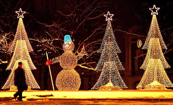 A man walks in past illuminated installations in the shape of a snowman and Christmas