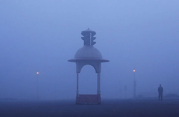 A man walks on a road amidst heavy fog on a winter morning in New Delhi