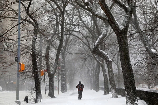 A man walks in the snow next to Central Park along 5th avenue in upper Manhattan during