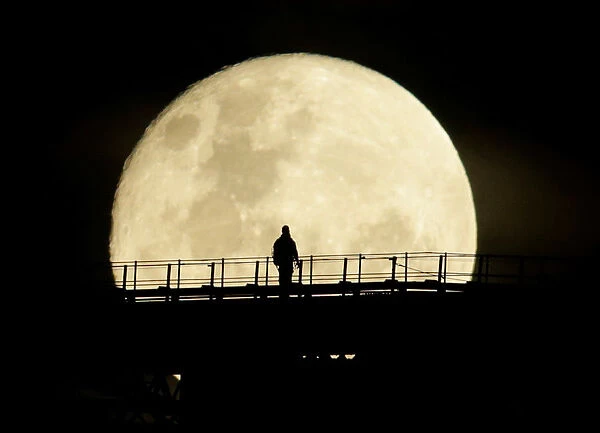 A man walks on the top span of the Sydney Harbour Bridge as the supermoon enters its