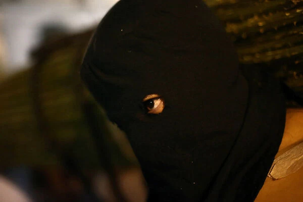 A masked penitent looks through the hole of his mask during a procession as part of Holy