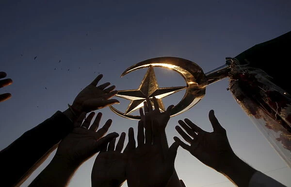 Men reach out to touch the emblems of a crescent moon and star, symbols representing Islam