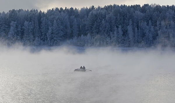 Two men row a boat through a frosty fog along the Yenisei River at air temperature some