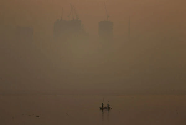 Men row a boat in the waters of the Arabian Sea on a smoggy evening in Mumbai