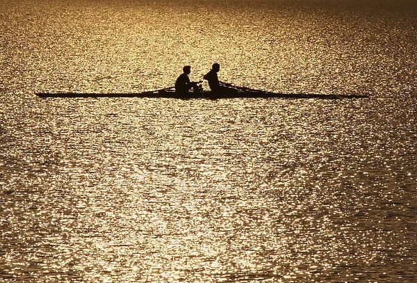 Men are silhouetted in the rising sun as they row in the waters of Sukhana Lake in