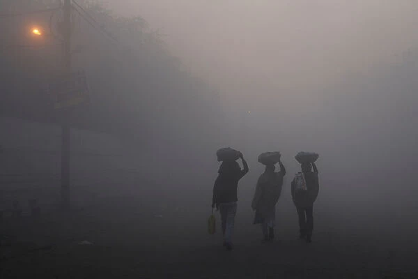 Men walk along a street on a foggy morning in the old quarters of Delhi