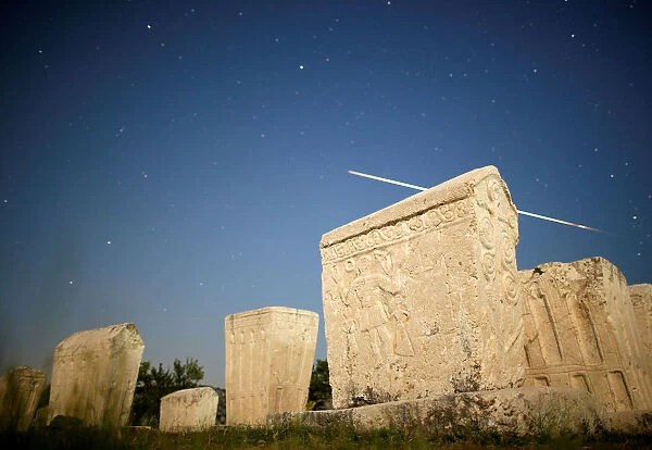 A meteor streaks past stars in the night sky above medieval tombstones during the