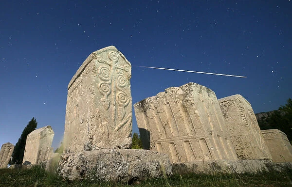 A meteor streaks past stars in the night sky above medieval tombstones during the Perseid