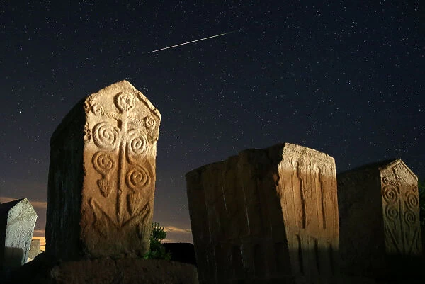 A meteor streaks past stars in the night sky above medieval tombstones in Radmilje near