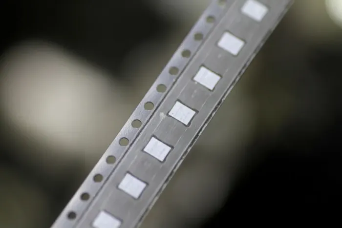 Framed Print : Microchips emerge from a machine onto a roll in the clean room at the UTAC plant in Framed Print : Microchips emerge from a machine onto a roll in the clean room at the UTAC plant in