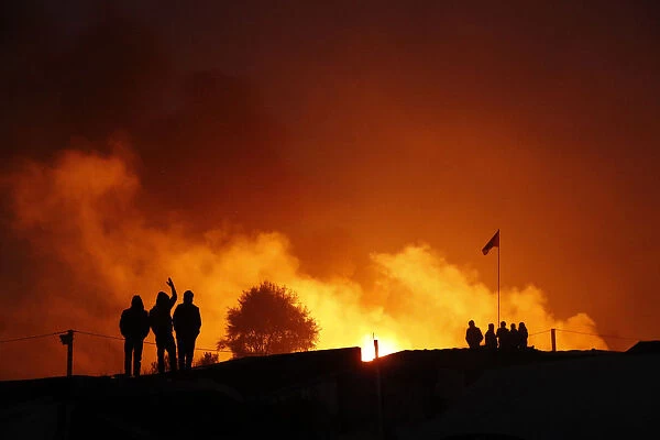 Migrants are seen in silhouette near flames from a burning makeshift shelter on the