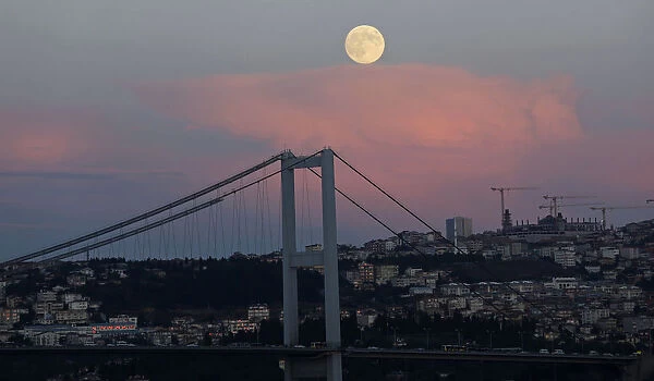 A full moon rises over the Bosphorus bridge in Istanbul