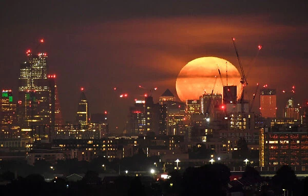 The full moon is seen rising behind skyscrapers at Canary Wharf and the London skyline