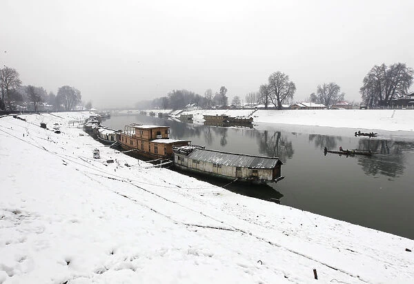 Moored houseboats are seen along the Jehlum river as Kashmiri fishermen row boats during