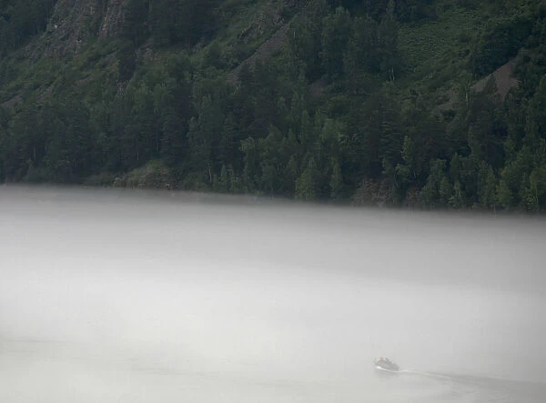 A motor boat sails through a low, fog-blanketed Yenisei River